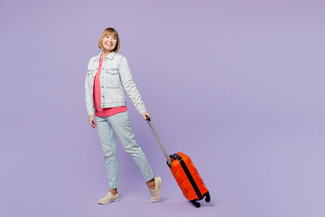 Traveler happy elderly woman 50s years old wears casual clothes hold valise isolated on plain pastel purple background. Tourist travel abroad in free spare time rest getaway. Air flight trip concept.