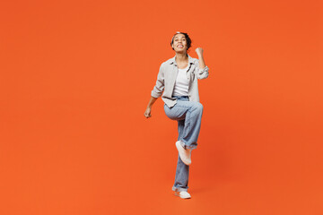 Fototapeta na wymiar Full body young woman of African American ethnicity she wears grey shirt headband doing winner gesture celebrate clenching fists say yes isolated on plain orange background. People lifestyle concept.