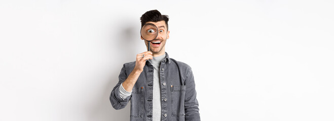 Happy funny guy look through magnifying glass with big eye, checking out interesting deal,...