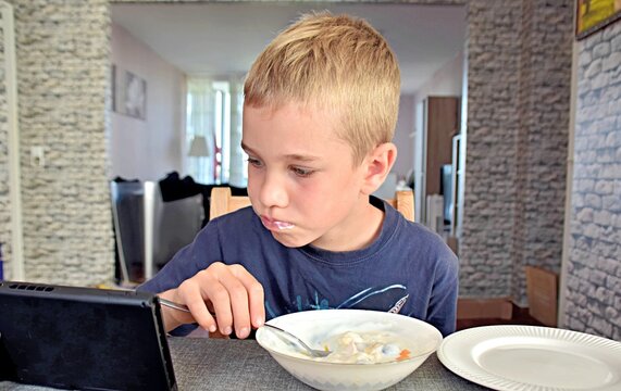 boy eats yogurt with fruit and looks into the gadget