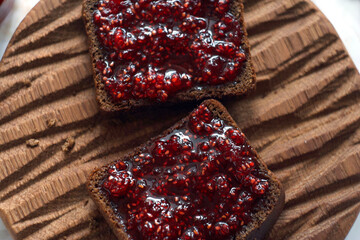 Two sandwiches with raspberry jam lie on a wooden board on a marble table. High angle view