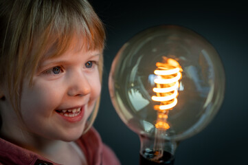 Happy child looks curious to a huge filament light bulb. Symbol for a happy child discovering the world.