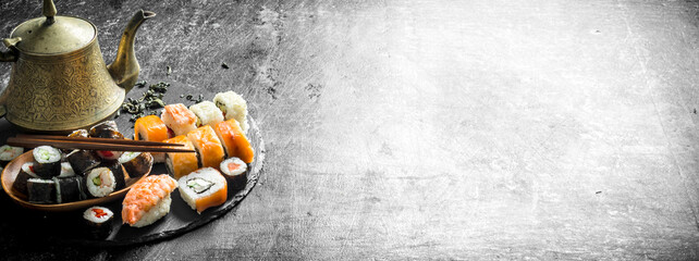 Rolls and maki on a stone stand with green tea in the teapot.