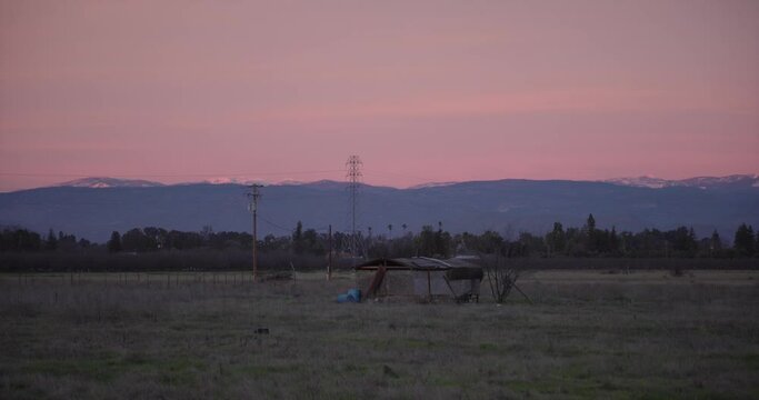 A pastel sky over the Sierra Nevada mountains with power lines and a shed in the foreground in Clovis, CA, USA