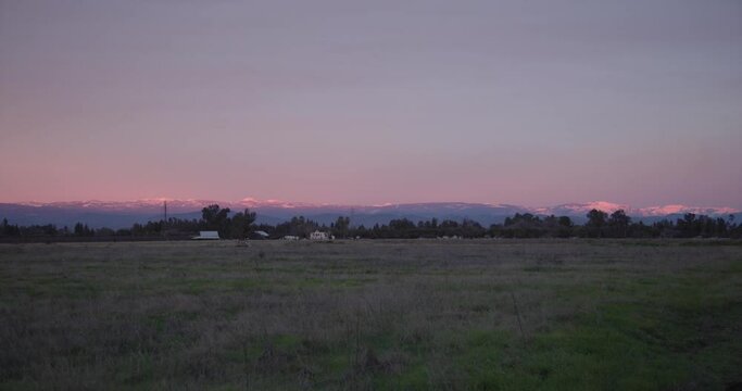 A pastel sky over the Sierra Nevada mountains with power lines and a farm, in the foreground in Clovis, CA, USA