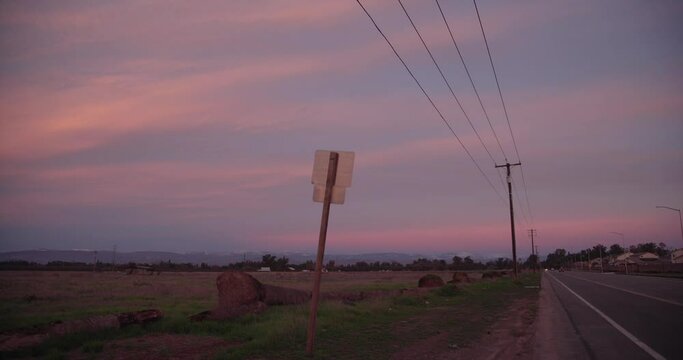 A pastel sky over the Sierra Nevada mountains with power lines and a road and traffic sign in the foreground in Clovis, CA, USA