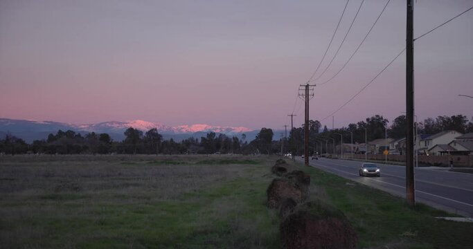 A pastel sky over the Sierra Nevada mountains with power lines a road, and fallen palm trees in the foreground in Clovis, CA, USA