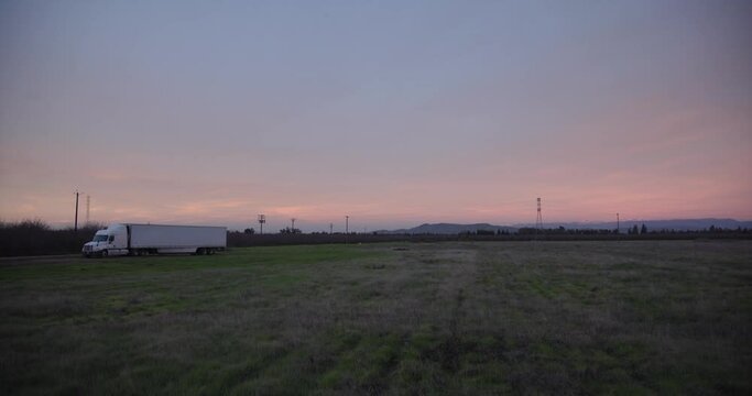 A pastel sky over the Sierra Nevada mountains with power lines and a 18 wheel truck in the foreground in Clovis, CA, USA
