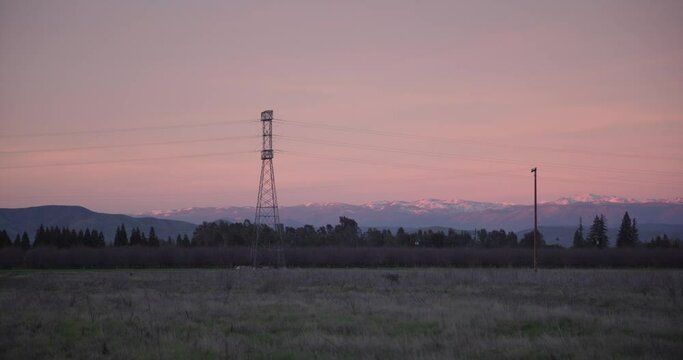 A pastel sky over the Sierra Nevada mountains with power lines and trees, in the foreground in Clovis, CA, USA