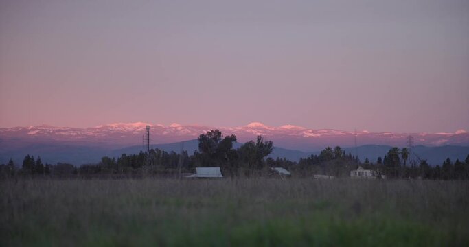 A pastel sky over the Sierra Nevada mountains with power lines, a farm and trees, in the foreground in Clovis, CA, USA