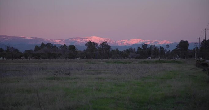 A pastel sky over the Sierra Nevada mountains with power lines and trees, in the foreground in Clovis, CA, USA