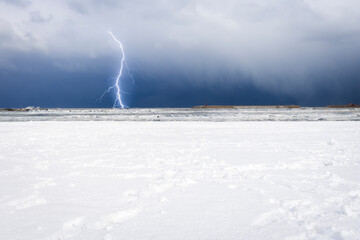 Scenic winter landscape of a snowstorm with lightning on deserted beach covered by snow with some...