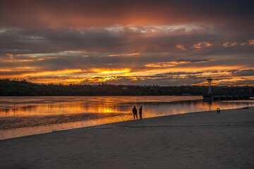 Two people are sitting on the bank of the river in contemplation of the sunset