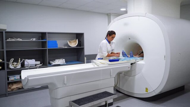 Medic standing near magnetic resonance imaging (MRI) scanner preparing the tools. Patient lies inside the machine.