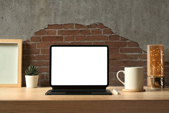 Front view of digital tablet with wireless keyboard, coffee cup, books and picture frame on wooden working desk