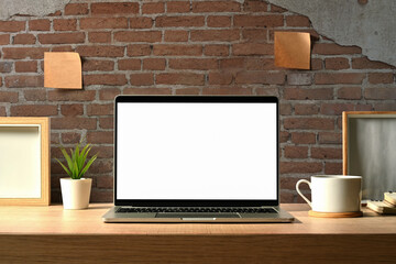 Front view of laptop computer with blank screen , houseplant, coffee cup and books on wooden table
