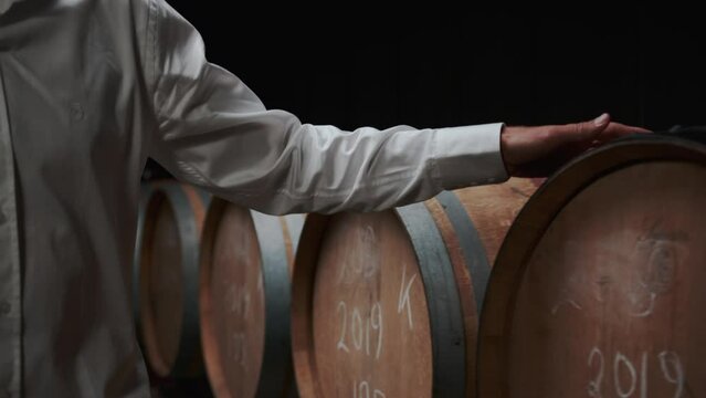 Male owners hand on Wooden oak whiskey, wine, cognac, brandy or beer barrels. A Wine Cellar. Storage Room for Wine in Bottles and Barrels.