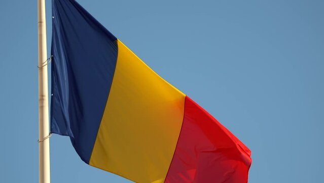 National flag of Romania. 4K video with Romanian flag waving against blue sky clear background in slow motion.