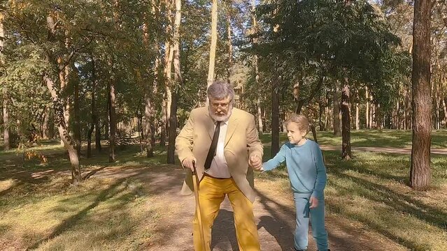 Little girl is rollerblading in the park, her old grandfather is holding her hand. Grandfather runs after the child on roller skates.