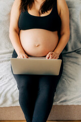 Unrecognizable pregnant business woman working at home on a laptop.