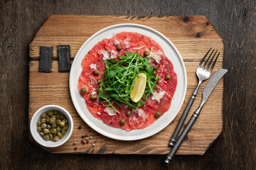Beef carpaccio with capers, arugula and parmesan on wooden background, flat lay
