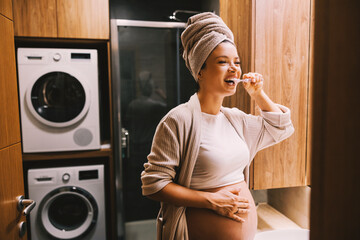 A pregnant woman is brushing her teeth in bathroom. Night time routine.
