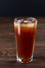 Non-alcoholic drink with ice in a tall glass on a brown wooden table.