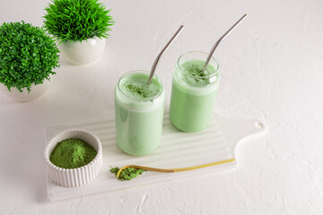 two modern glasses in the form of a beer can with green tea matcha latte on a white board with a bowl of green matcha powder. natural organic drink.