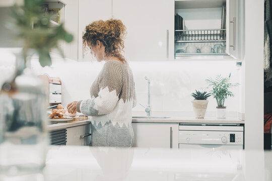 One woman alone in the kitchen in real life preparing food for lunch. Single lady lifestyle concept. White home interior minimal style. Indoor leisure activity cooking for dinner.