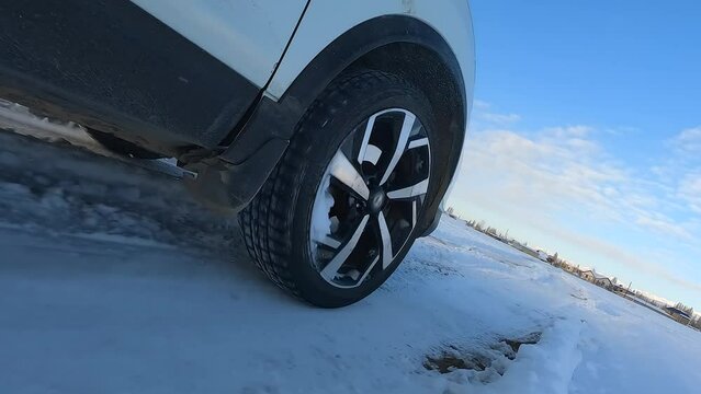 Close-up on the right front wheel of the SUV. A white car is driving through a snowy field. Traveling by car in winter. The littered horizon is like a dynamic reception. An exciting road adventure.