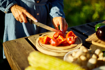 Unrecognizable woman cutting fresh pepper vegetables on wooden board