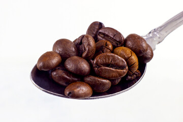 Dark brown roasted coffee beans in a spoon on white background close up.