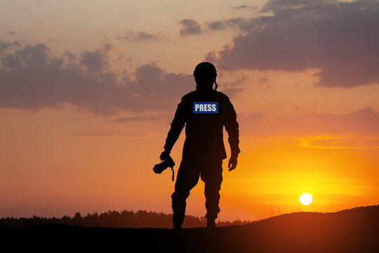 Photojournalist silhouette documenting war or conflict. Photojournalist at sunset. War, army, technology and journalist work concept.