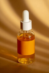 Orange serum in transparent glass bottle with a white dropper cap close-up on brown background in sunlight. Mock up of essential oil for care of women's skin. Concept of beauty. Vertical image