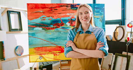 Portrait of cheerful young Caucasian beautiful talented woman artist in apron standing in studio...