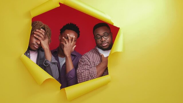 Facepalm gesture. Skeptic black men. Epic fail. Displeased male friends looking from yellow disrupted paper hands on forehead on red background copy space.