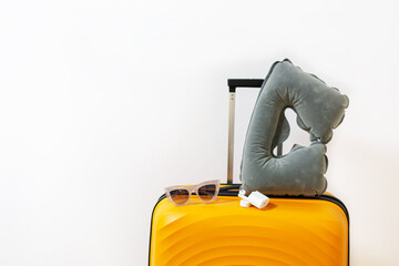 Close up orange suitcase inflatable pillow, sunglasses, white headphones on a white wall background...