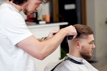 Fototapeta premium Barber trim hair with clipper on handsome bearded man
