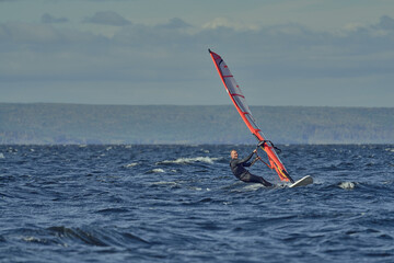 A mature man, an experienced windsurfer, rushes along the surface of the water, splashes scatter to...