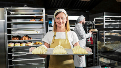 Portrait shot of beautiful female in white apron and hat standing in front of camera, holding tray...