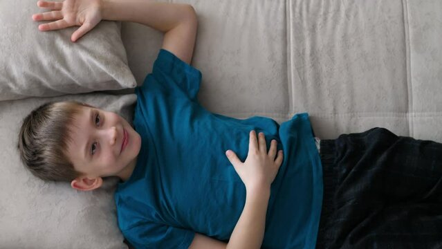carefree caucasian boy 8-9 years old jumps on the sofa to rest on the pillow.the child is resting on the sofa at home, top view. lifestyle schoolboy at home