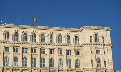 Flag of Romania waving on top of Palace of Parliament landmark building from Bucharest during a sunny day with blue sky. Travel to Bucharest.