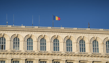 Flag of Romania waving on top of Palace of Parliament landmark building from Bucharest during a sunny day with blue sky. Travel to Bucharest.