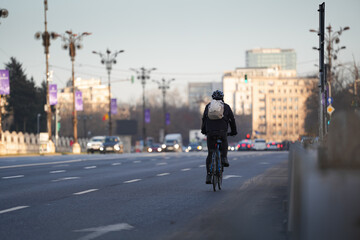 Going to work by bike. Photo with a biker from behind commuting to work on a bike in the middle of a city. Eco friendly transportation concept image.