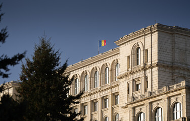 Flag of Romania waving on top of Palace of Parliament landmark building from Bucharest during a sunny day with blue sky. Travel to Bucharest.