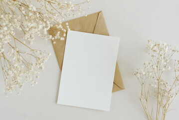 Greeting card mockup, envelope and  dried gypsophila flowers twigs on beige background top view flatlay. Card mockup with copy space.