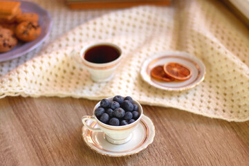 Plate of cookies, cup of tea, fresh blueberries, dry oranges, stack of books, reading glasses and tablet on the table. Hygge at home. Selective focus.