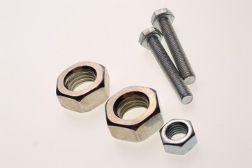 New, chrome-plated bolts and nuts of different sizes lie on a white background. Close-up