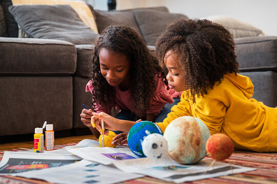 Sisters Making Solar System For Science Project In Living Room At Home