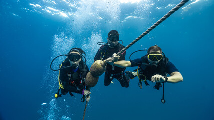 three professional diver checking his dive computer to ascend safely. holding on to a rope